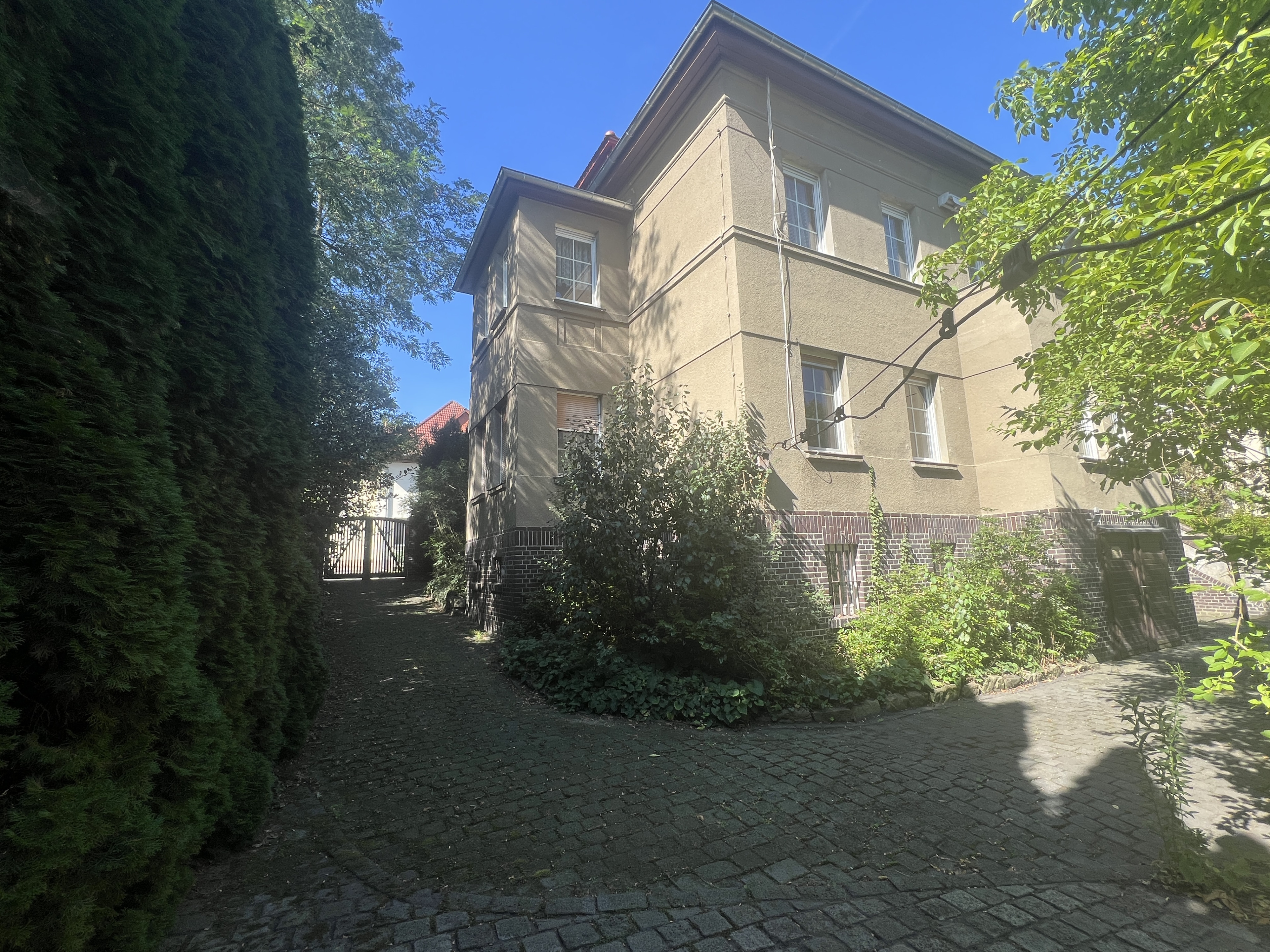 Zweistöckiges Wohnhaus mit gepflasterter Einfahrt und Garten an einem sonnigen Tag