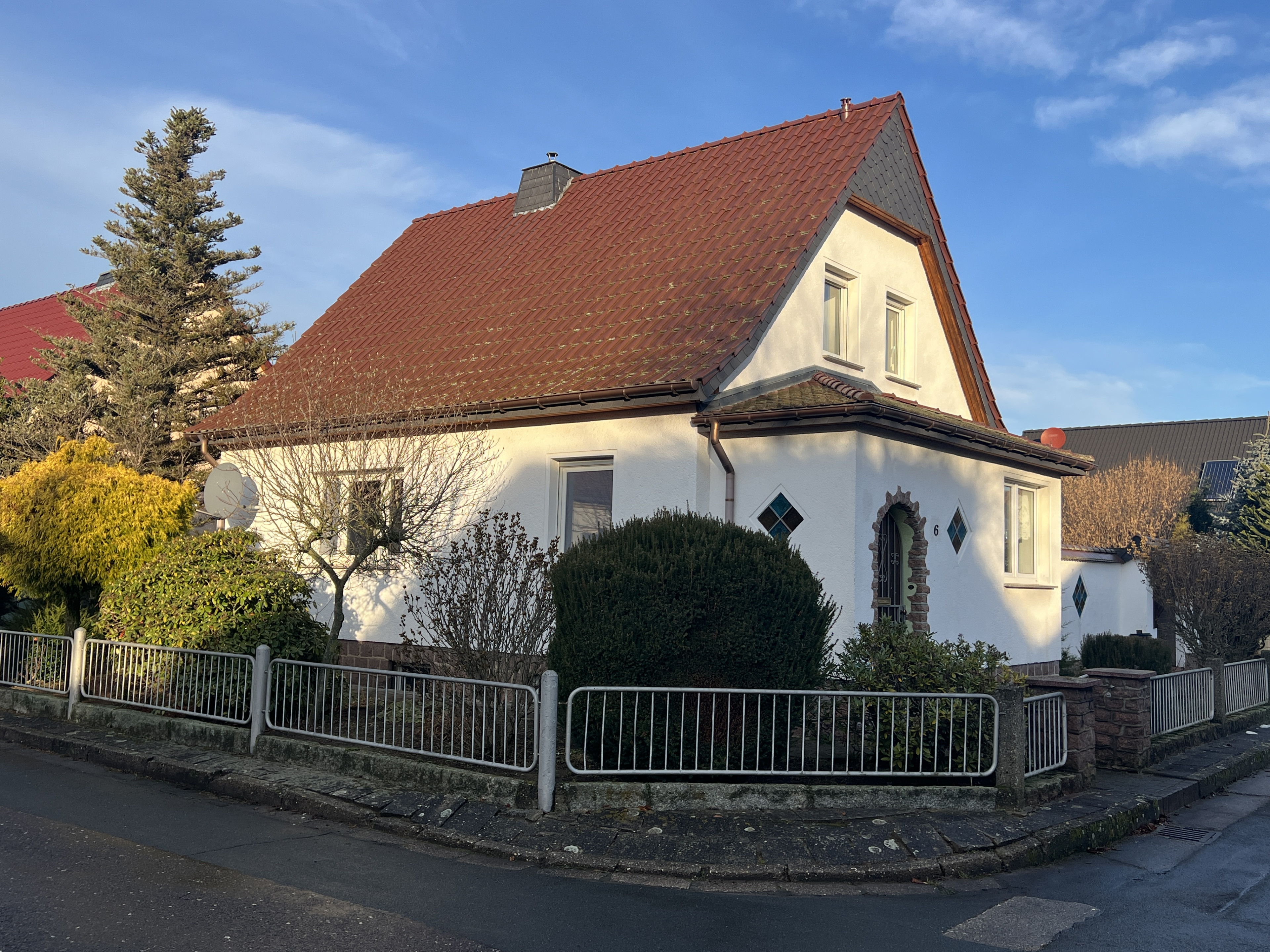 Einfamilienhaus mit rotem Satteldach und gepflegtem Vorgarten an einer Straßenecke