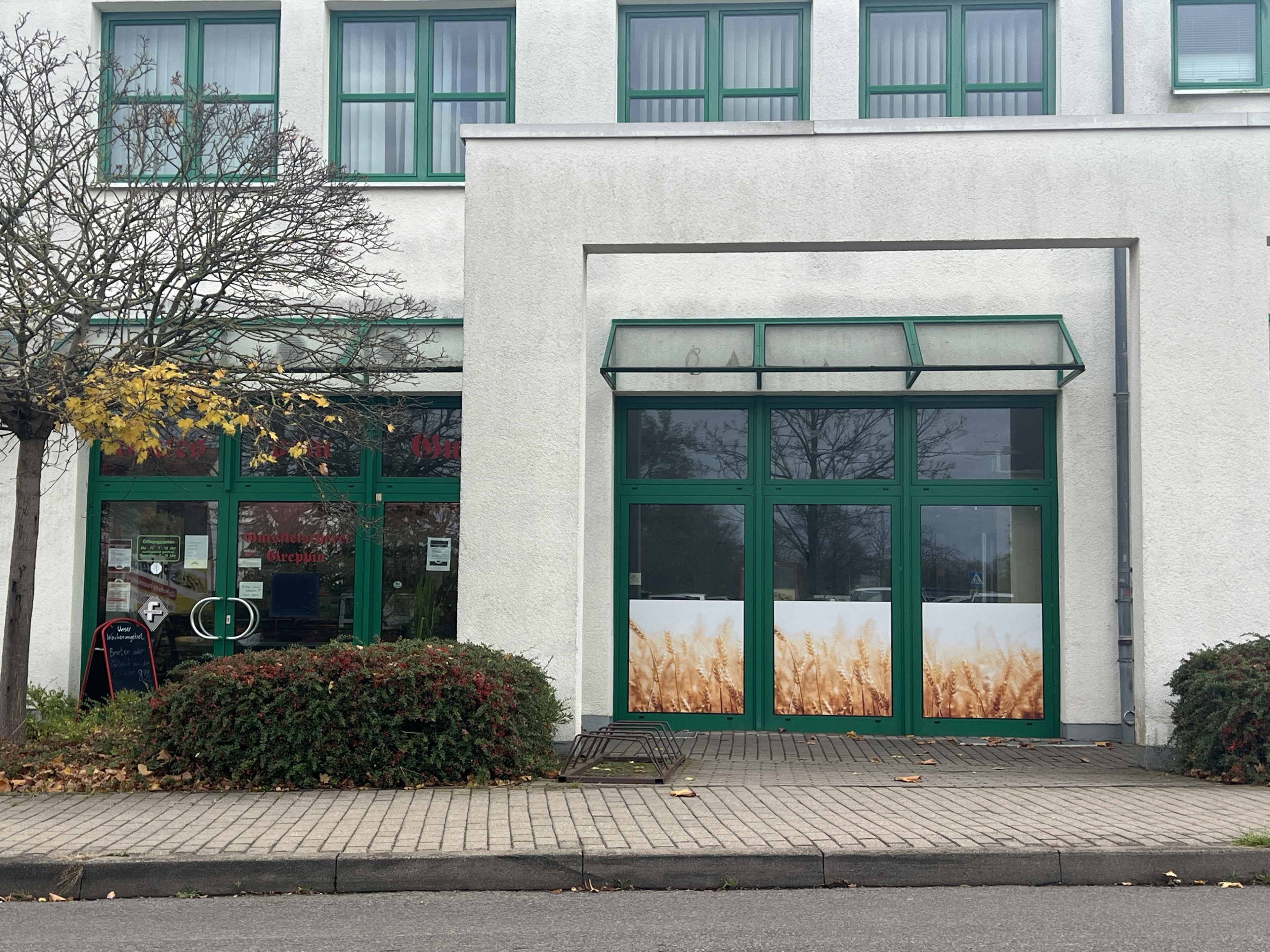 Titelbild einer Bäckerei mit grünem Eingangsbereich und Fenstern, außen mit Weizenmotiv dekoriert