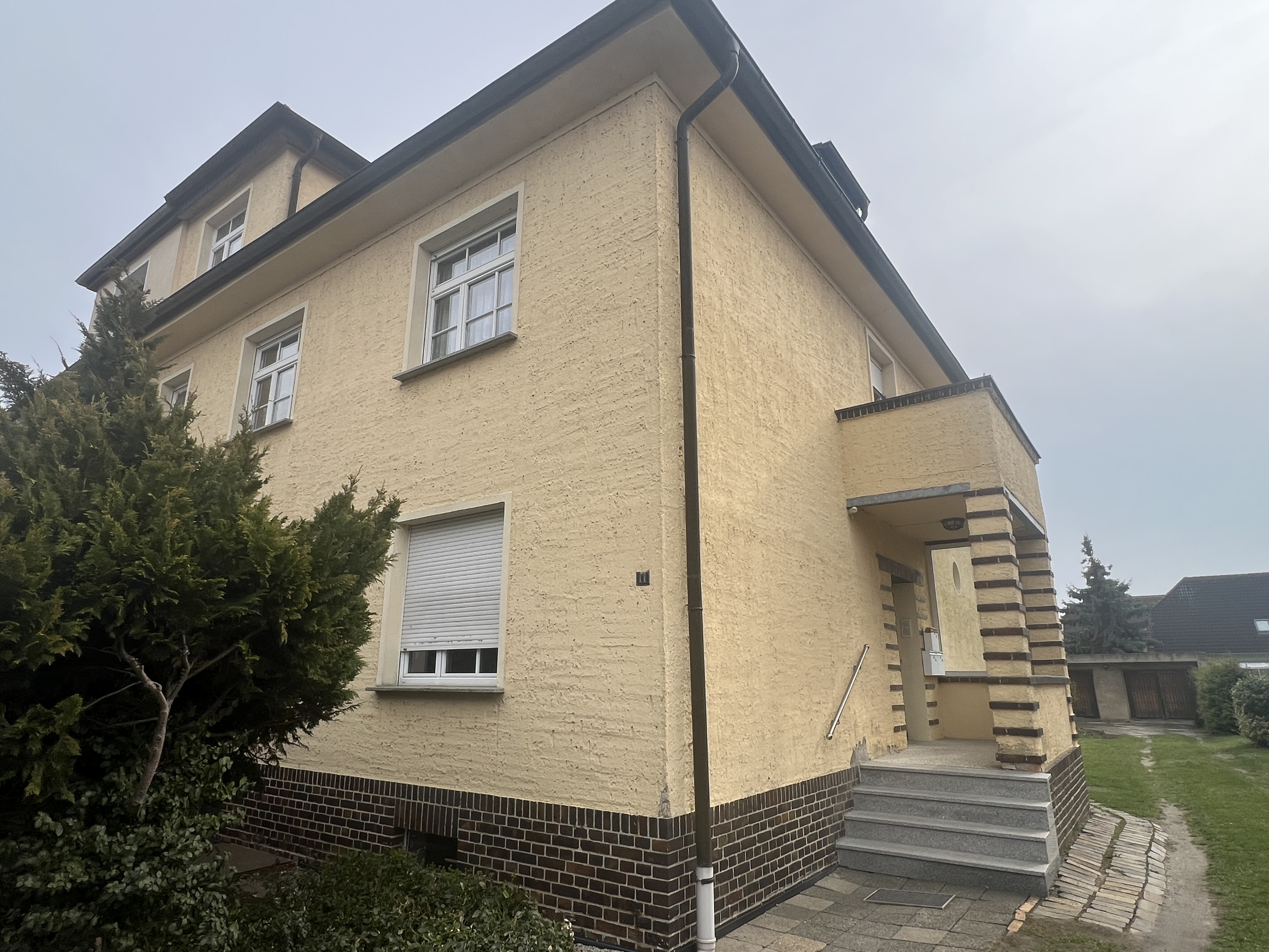 Titelbild eines gelben Einfamilienhauses mit Eingangsbereich und Treppe