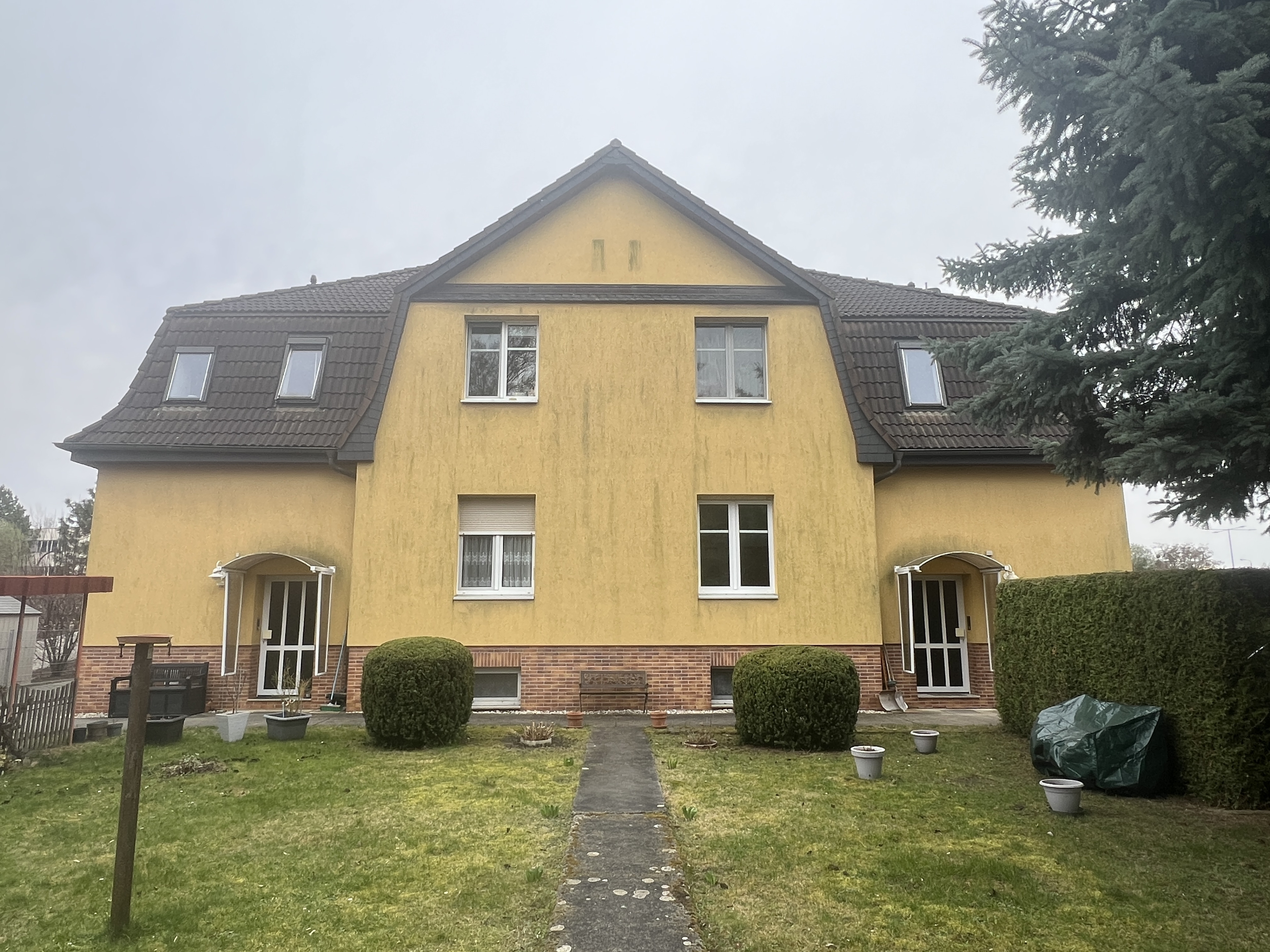 Mehrfamilienhaus mit gelber Fassade und gepflegtem Vorgarten