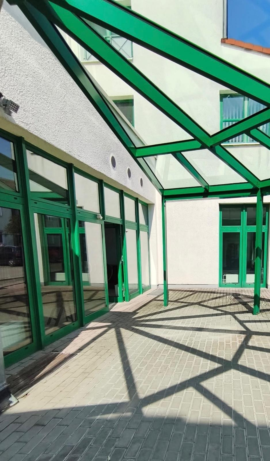 titelbild neu moderner Gebäudeeingang mit grünen Fensterrahmen und Glasüberdachung