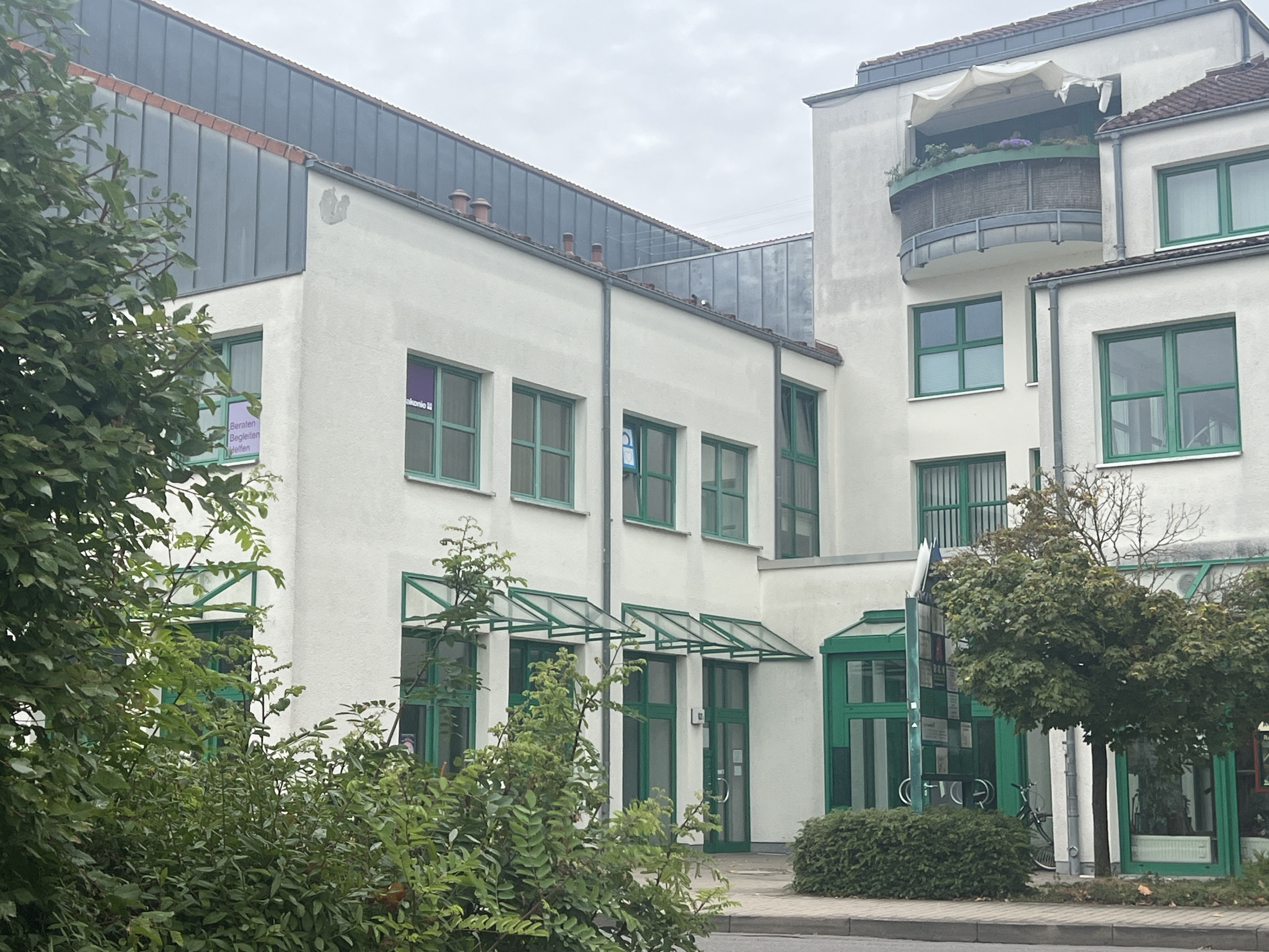 Modernes Bürogebäude mit grünen Fensterrahmen und Glasvordächern an einem bewölkten Tag