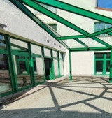 titelbild-neu: Moderner Gebäudeeingang mit grünen Fensterrahmen und Glasüberdachung