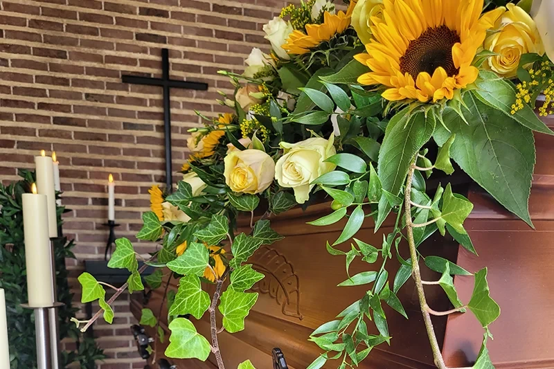 Bestattungen: Sarg mit Sonnenblumen und weißen Rosen als Trauerfloristik in einer Kapelle