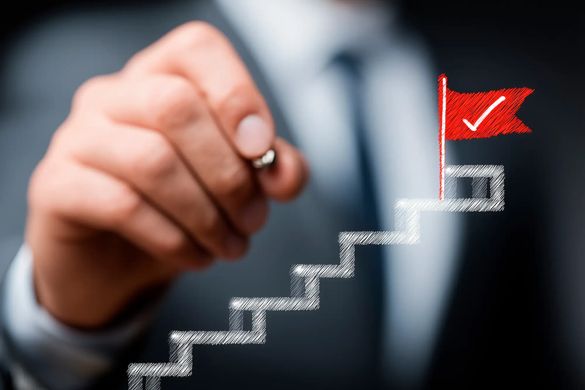 Betriebswirtschaft: Hand zeichnet Treppe mit Zielflagge als Symbol für wirtschaftlichen Erfolg