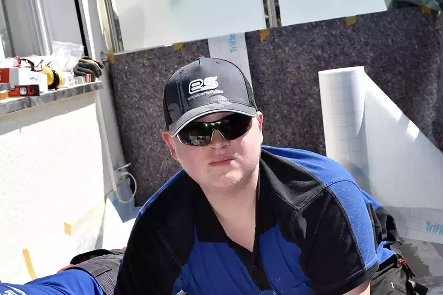 Dachdecker in blauer Arbeitskleidung mit Sonnenbrille und Mütze