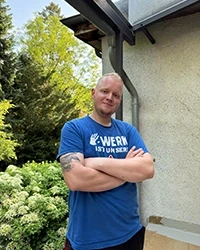 Person im blauen T-Shirt vor einem Haus und Bäumen Person im blauen T-Shirt vor einem Haus und Bäumen