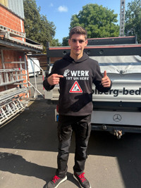 Person mit 'Werk ist unsere Stärke' Hoodie vor Handwerkerfahrzeug Person mit schwarzem Hoodie mit Aufdruck 'Werk ist unsere Stärke' vor einem Handwerkerfahrzeug