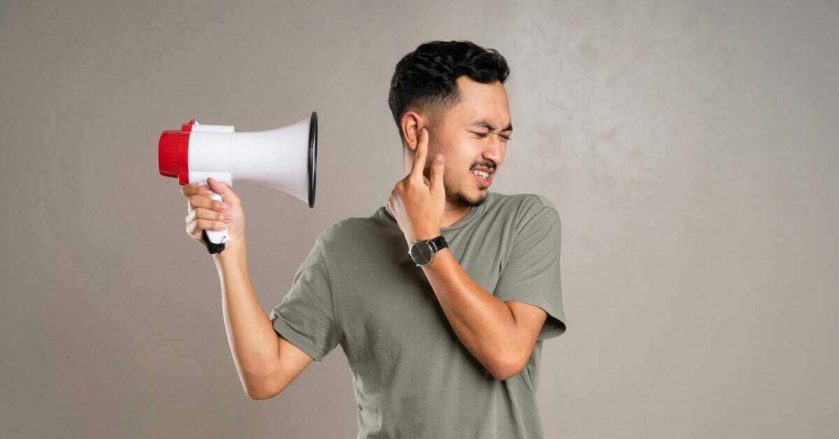 Mann hält sich die Ohren zu wegen nervigem Lärm durch ein Megafon