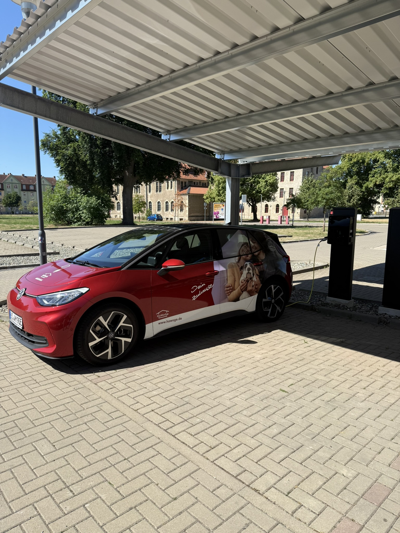 Rotes Elektroauto mit Hawoge-Werbung an einer Ladestation Rotes Elektroauto an einer Ladestation mit Hawoge-Werbung