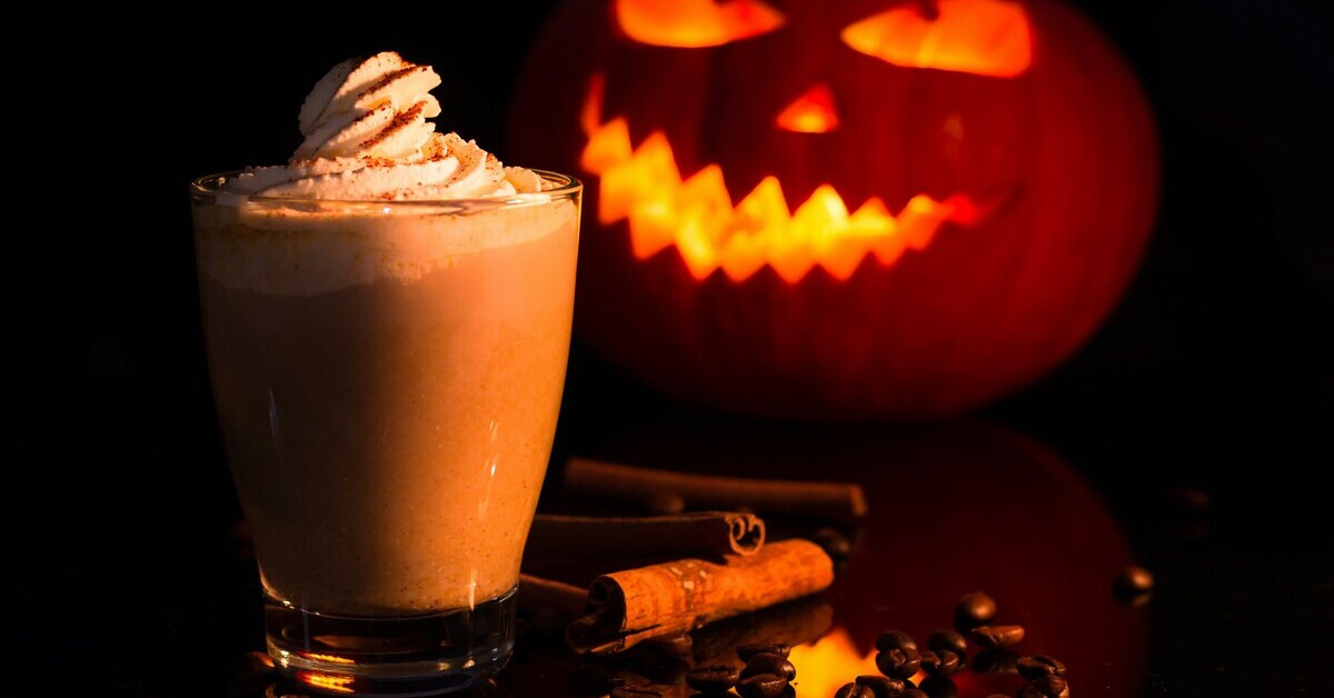 Halloween-Getränk mit Sahne und Zimt vor leuchtendem Kürbis
