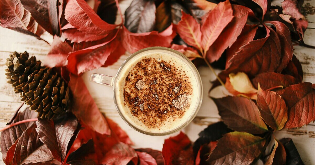 Herbstgetränk mit Zimt in einer Tasse, umgeben von bunten Herbstblättern