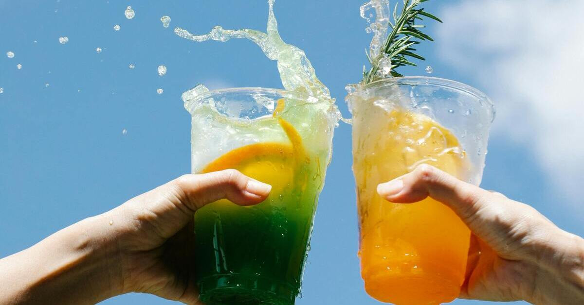 Zwei Personen stoßen mit Fassbrause an, erfrischende Sommergetränke vor blauem Himmel