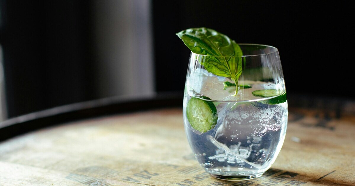 Gin mit Basilikum und Gurke in einem Glas auf einem Holztisch