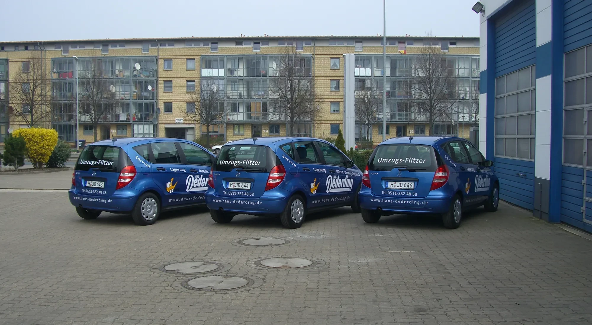 Drei blaue Umzugs-Flitzer Fahrzeuge von Dederding vor einem Wohnhaus