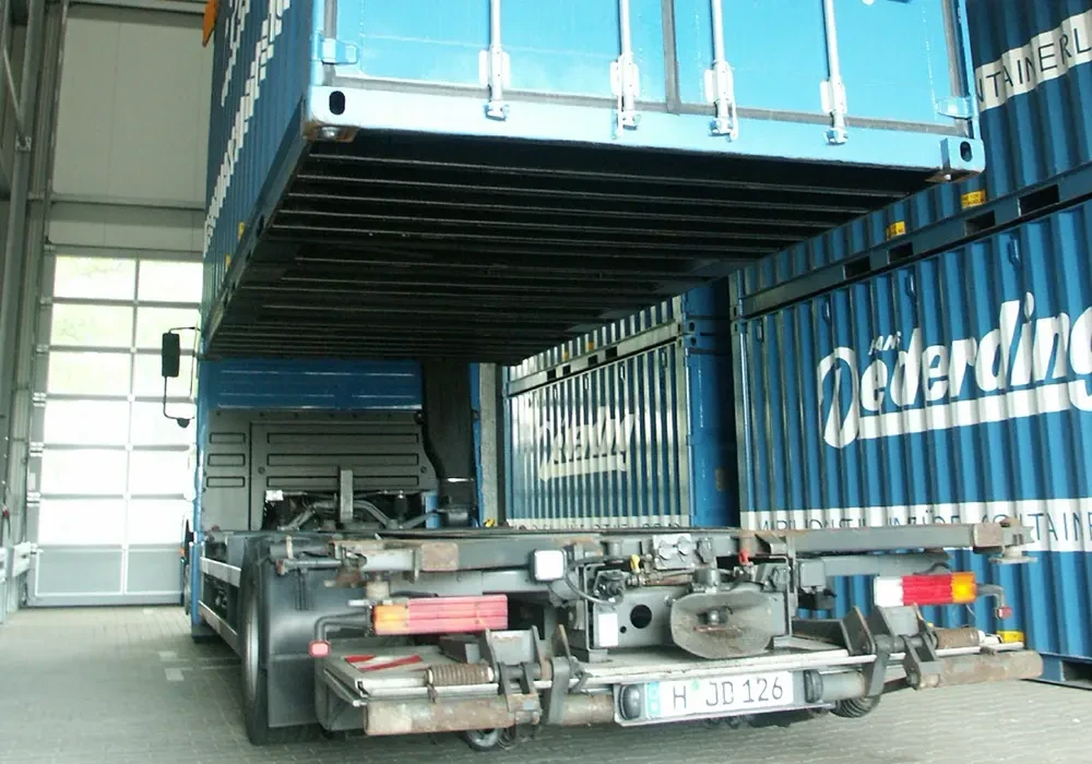 Containerhalle und LKW-Transporte mit blauen Containern beim Be- oder Entladen