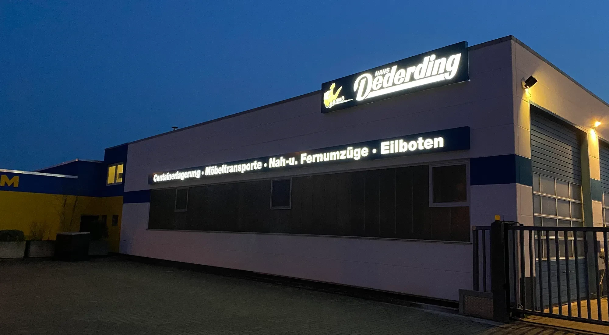 Beleuchtetes Firmengebäude von Hans Dederding mit Hinweis auf Eilboten, Möbeltansporte und Fernumzüge