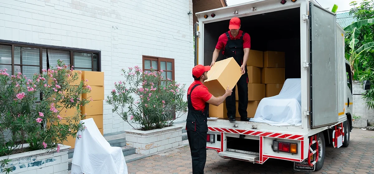 Umzugshelfer laden Umzugskartons aus einem Transporter vor einem Haus aus