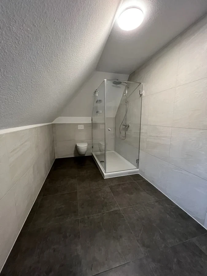 Modernes Badezimmer nach der Badsanierung mit Dusche und Wand-WC unter Dachschräge