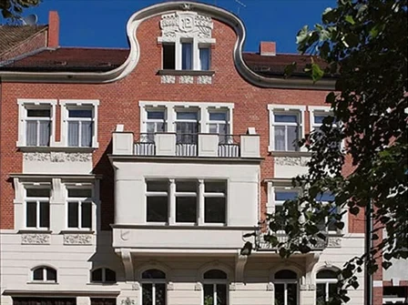 Großes Haus mit roter Ziegelsteinfassade und dunkelrotem Dach unter blauem Himmel