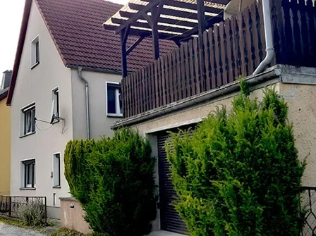 Beiges Haus mit braunem Dach und zwei Büschen