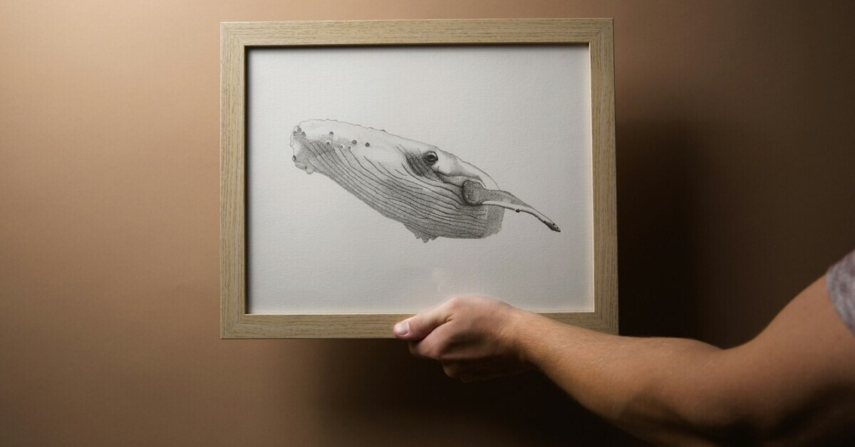 Kunst an der Wand: Hand hält gerahmte Zeichnung eines Wals vor brauner Wand