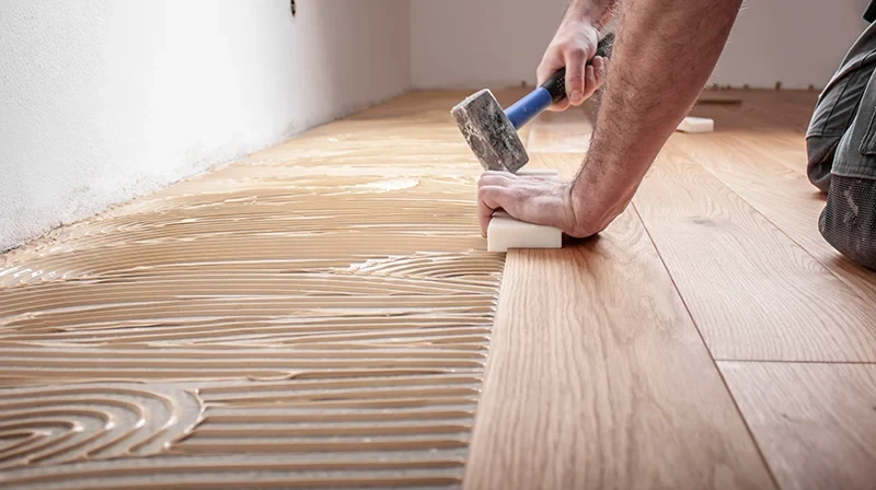 Verlegen von Bodenbelägen – Handwerker verlegt Holzboden mit Werkzeug