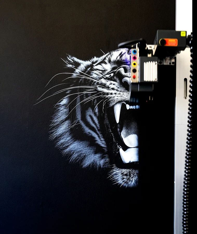 Wanddrucker druckt ein realistisches Tiger-Motiv auf eine schwarze Wand