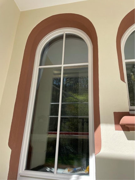 Malerarbeiten an einem Fenster mit brauner Umrahmung und frisch gestrichener Fassade