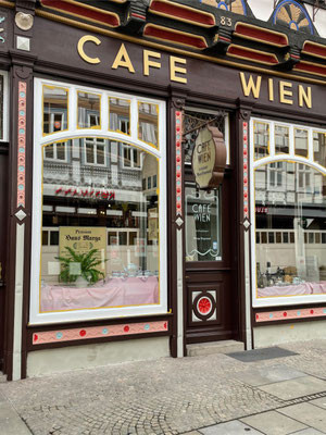Fassadenansicht eines Cafés nach professionellen Malerarbeiten, dekorative Fensterrahmen und Beschriftung Café Wien
