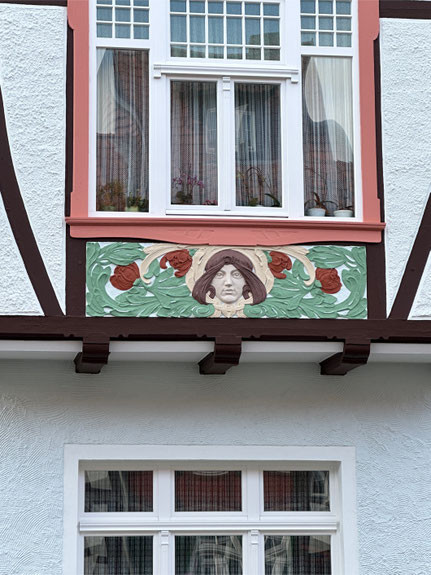 Detail einer Fassadenmalerei mit floralen Elementen und einer Frauenfigur unter einem Fenster – Beispiel für Malerarbeiten an einer Fachwerkfassade
