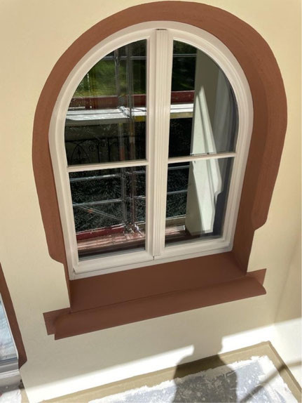 Malerarbeiten an einem Fenster mit brauner Umrahmung und weißem Fensterrahmen