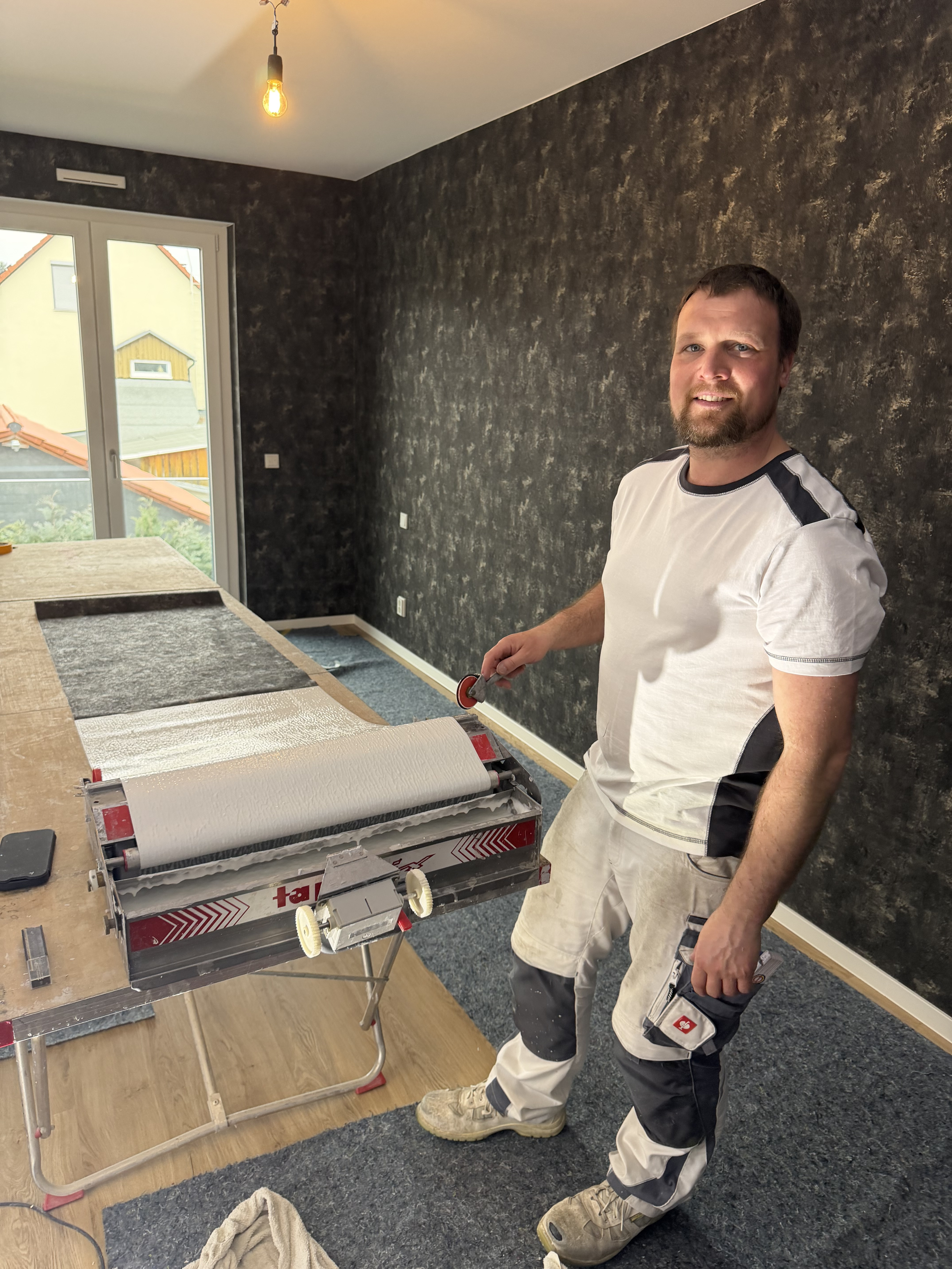 Handwerker beim Tapezieren einer Wand mit Tapeziermaschine in modernem Raum