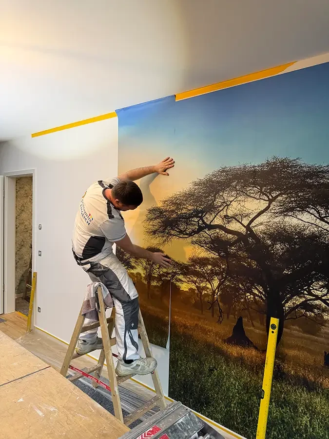 Handwerker bringt Wandbild mit Afrika-Motiv an einer Wohnzimmerwand an