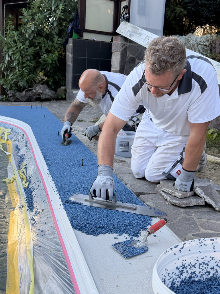 Handwerker bei der Verarbeitung einer Poolumrandung mit blauen Steinen
