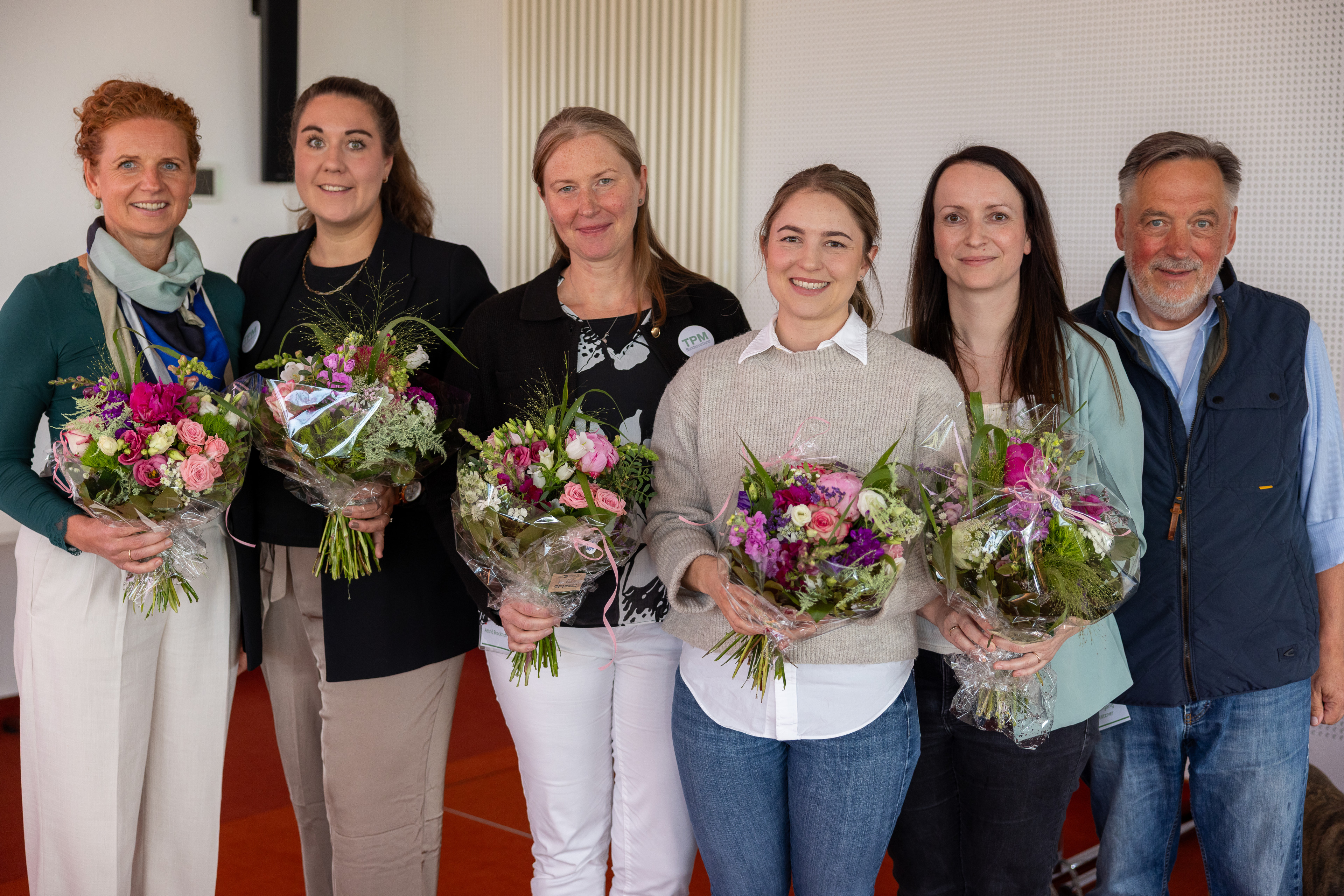 Vier Frauen halten Blumensträuße in einem Raum.