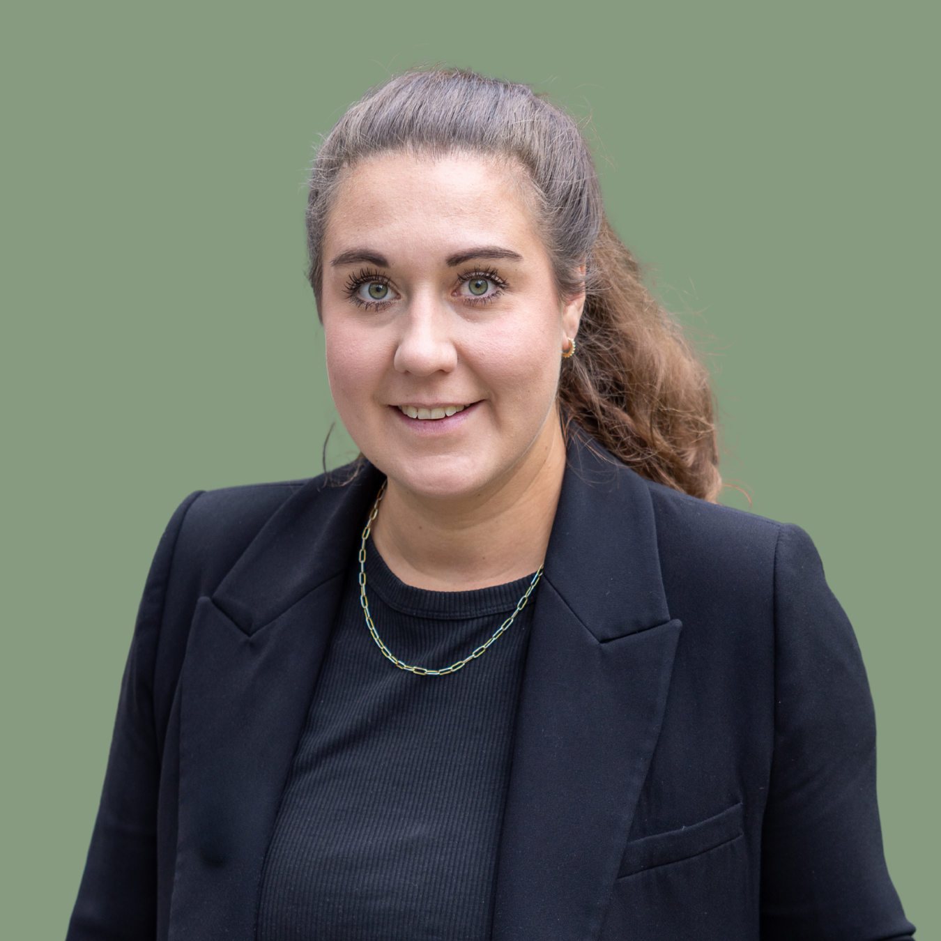 Frau mit braunen Haaren im schwarzen Blazer vor grünem Hintergrund