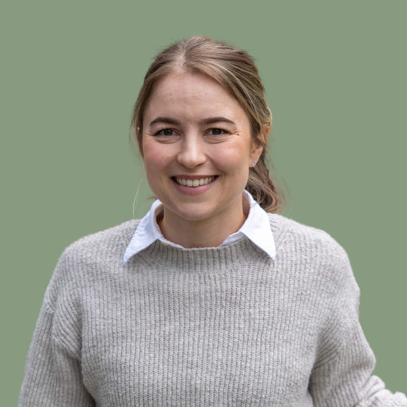 Frau mit grauem Pullover und weißem Hemd vor grünem Hintergrund