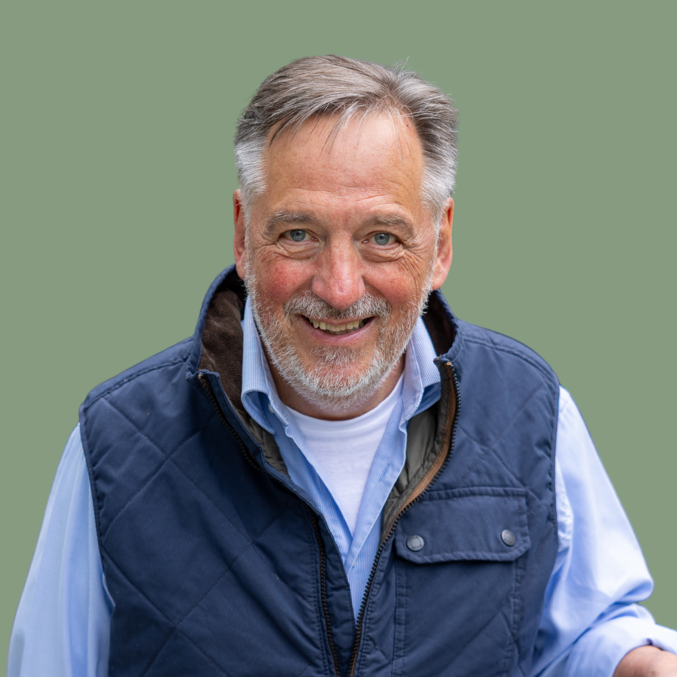Mann mit grauen Haaren und blauer Weste vor grünem Hintergrund