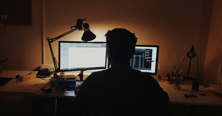 Mann am Bildschirm im Dunkeln arbeitet nachts am Computer