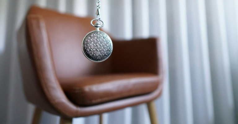 Hypnose mit Taschenuhr vor einem Sessel im Therapieraum