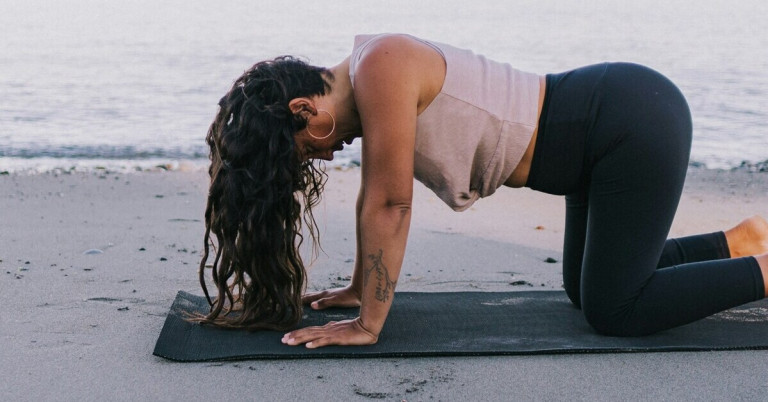 Kuh Yogahaltung (Bitilasana) – Yoga am Strand Frau macht die Yogahaltung Kuh (Bitilasana) am Strand auf einer Matte
