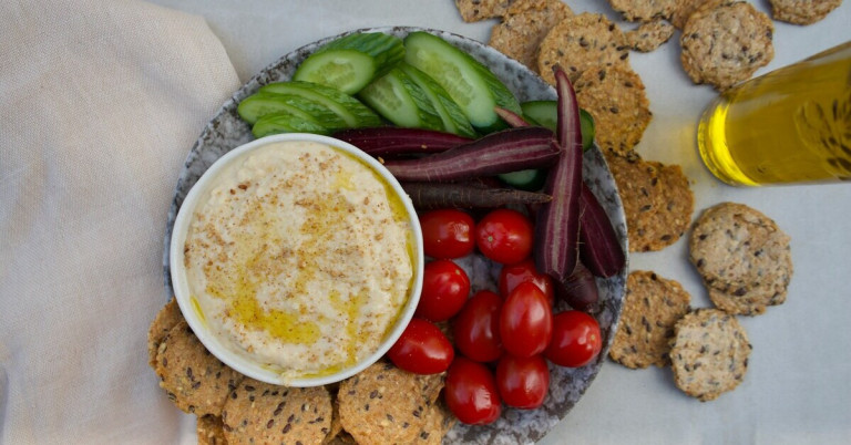 Hummus und Gemüse Snack mit Gurken, Karotten, Tomaten und Crackern auf einem Teller