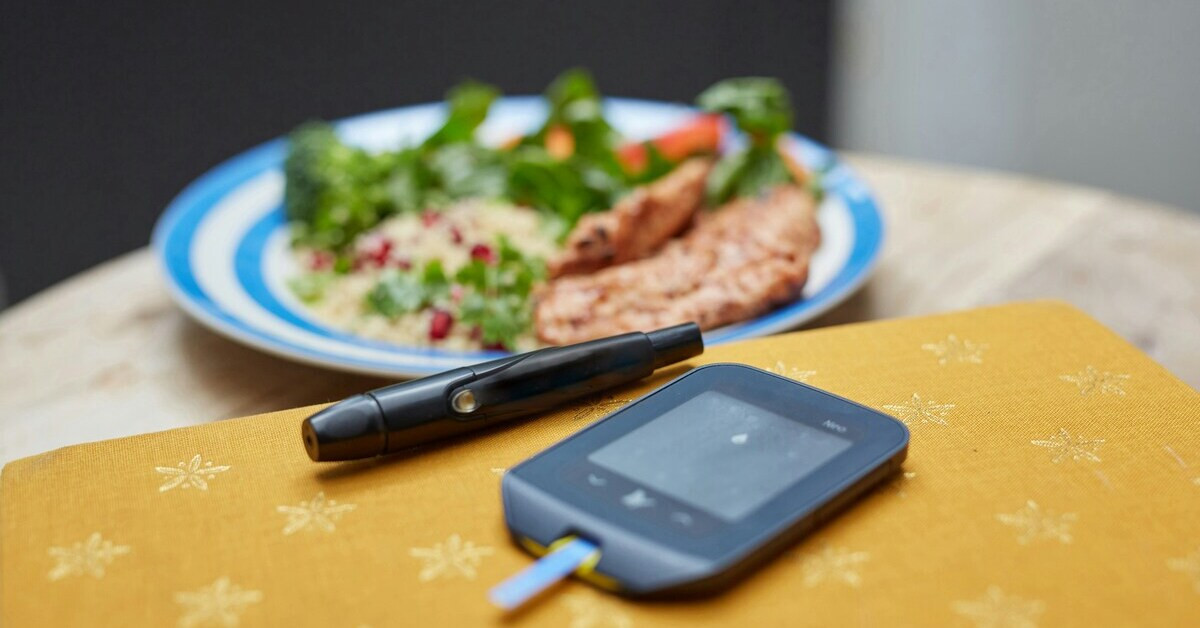 Blutzuckermessgerät und Stechhilfe auf Tisch mit gesundem Essen im Hintergrund