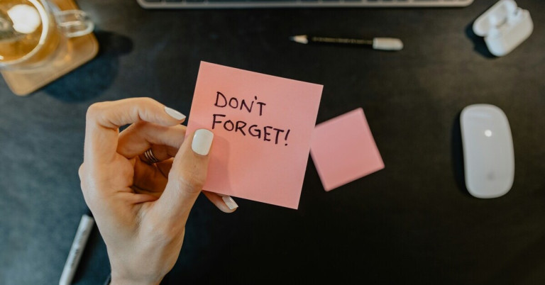 Hand hält pinken Notizzettel mit der Aufschrift 'Don't forget!'