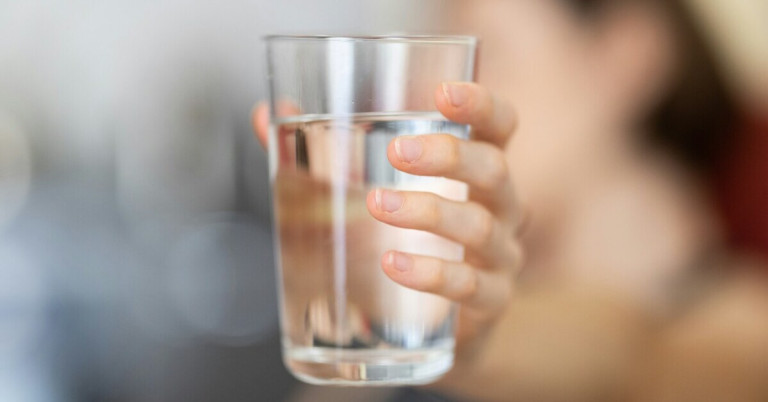 Hand hält ein Glas Wasser