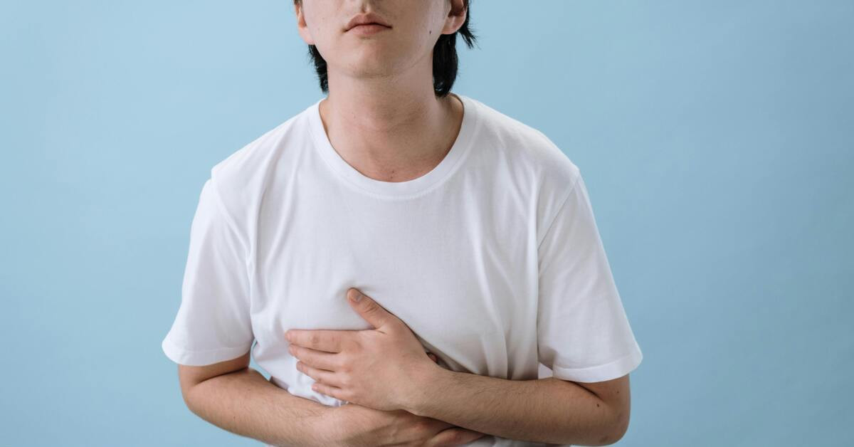 Mann mit Magenschmerzen hält sich den Bauch vor blauem Hintergrund