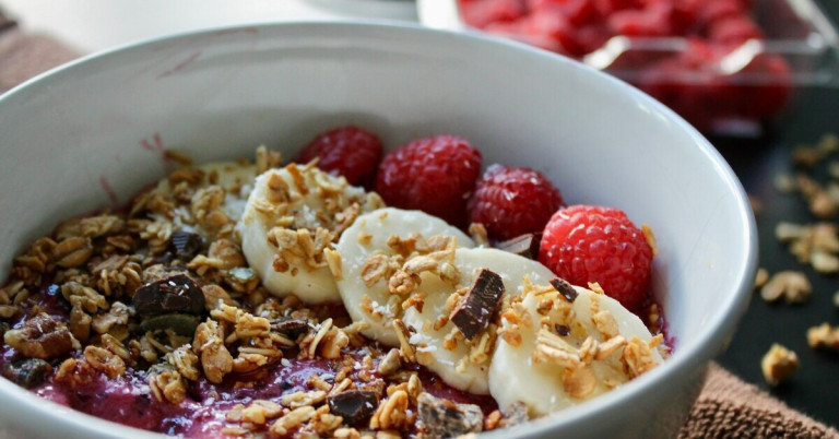 Schale mit Cerealien und Obst – gesundes Frühstück mit Bananen, Himbeeren und Müsli Schale mit Cerealien und Obst, darunter Bananenscheiben, Himbeeren und Müsli
