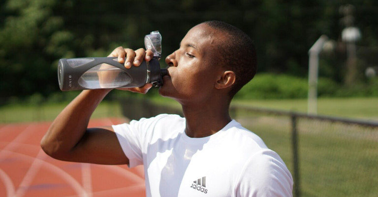 Sportler trinkt Wasser – Erfrischung beim Training auf der Laufbahn Sportler trinkt Wasser auf einer Laufbahn
